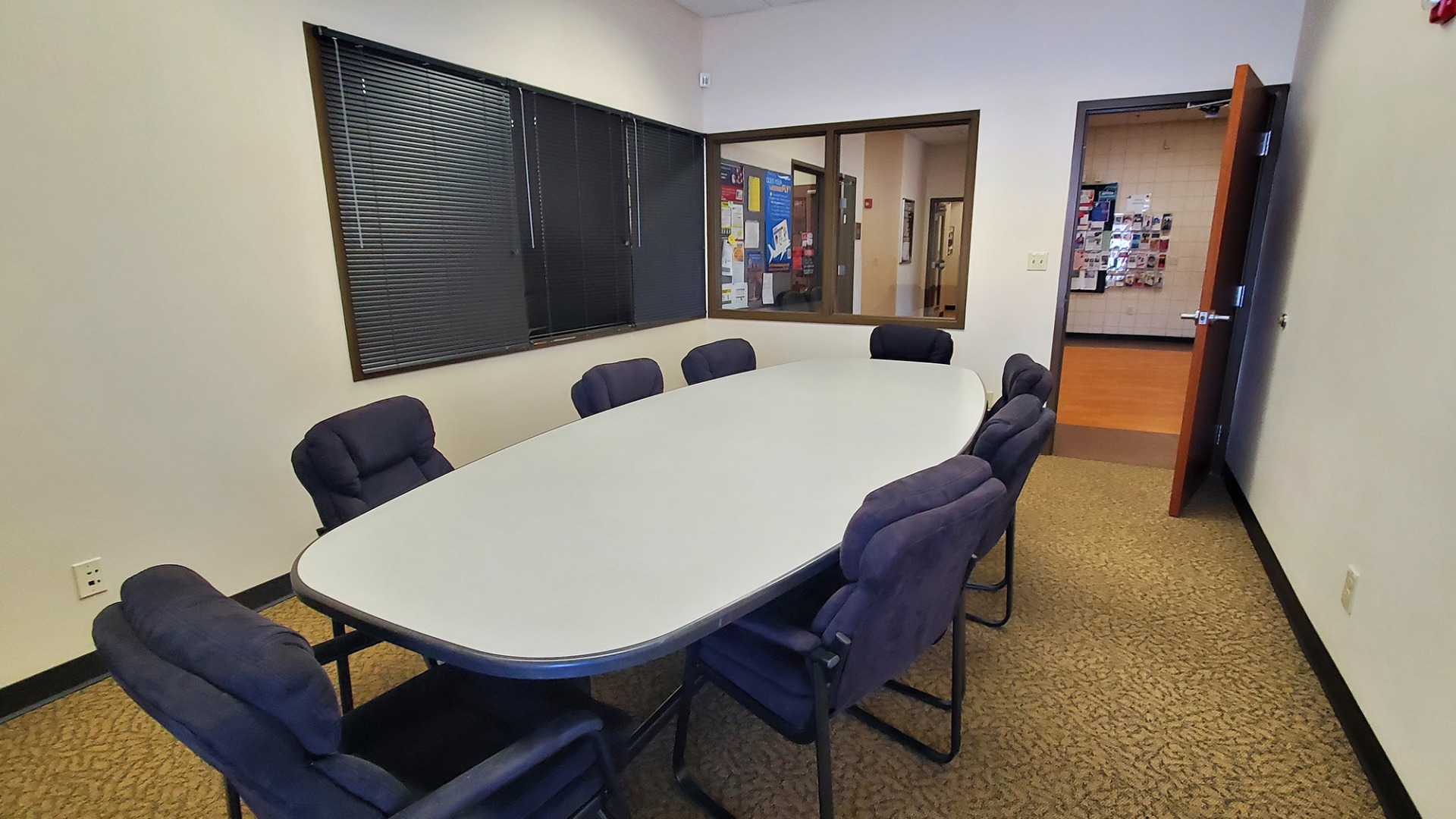 Room with inner and outer windows, large enough for its oval-shaped table surrounded by cushioned office chairs.
