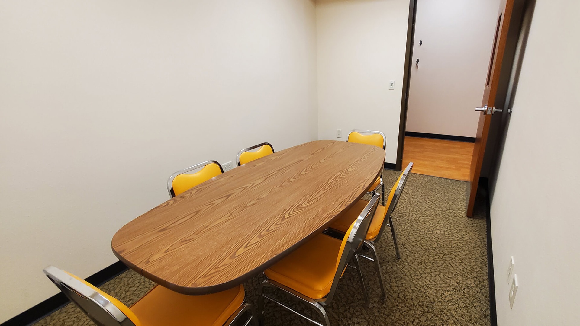 Meeting room with an oval-shaped table surrounded by six padded metal chairs.